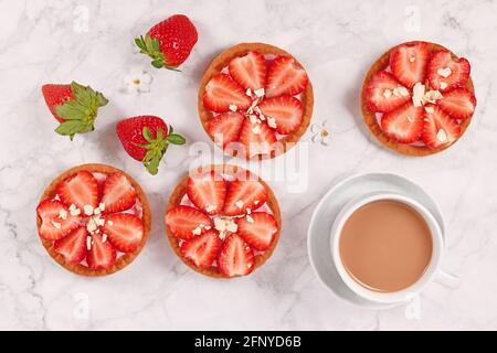 Petites pâtisseries tartelettes garnies de fruits à la fraise et de chocolat blanc saupoudrer à côté de la tasse à café Banque D'Images