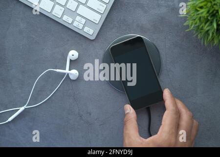 Homme chargé le smartphone à la main à l'aide du socle de chargement sans fil, vue du dessus Banque D'Images