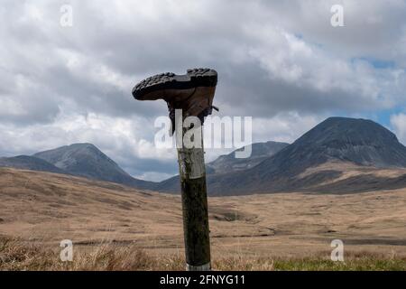 Une chaussure de marche jetée sur un poteau de signalisation routière avec les Paps du Jura au loin, île du Jura, Hébrides intérieures, Écosse. Banque D'Images