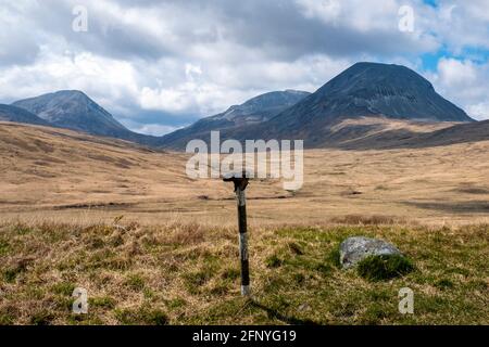 Une chaussure de marche jetée sur un poteau de signalisation routière avec les Paps du Jura au loin, île du Jura, Hébrides intérieures, Écosse. Banque D'Images