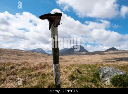 Une chaussure de marche jetée sur un poteau de signalisation routière avec les Paps du Jura au loin, île du Jura, Hébrides intérieures, Écosse. Banque D'Images