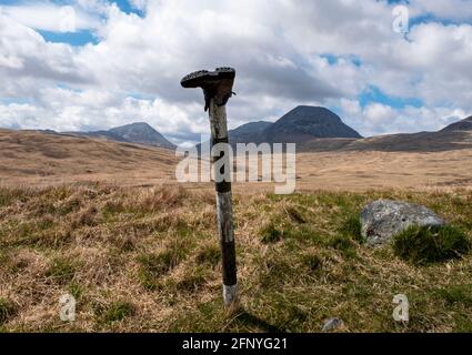 Une chaussure de marche jetée sur un poteau de signalisation routière avec les Paps du Jura au loin, île du Jura, Hébrides intérieures, Écosse. Banque D'Images