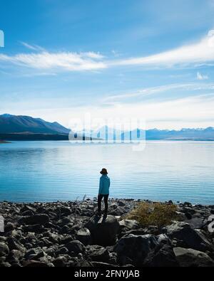 Femme debout sur les rives du lac Pukaki, bénéficiant de la vue sur le Mont Cook et les Alpes du Sud, sur l'île du Sud. Format vertical. Banque D'Images