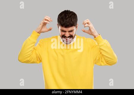 jeune homme en colère avec un sweat-shirt jaune sur le gris Banque D'Images