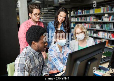 étudiants dans des masques médicaux avec ordinateur à la bibliothèque Banque D'Images