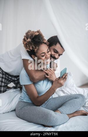 Homme embrassant une femme prenant le selfie sur le lit Banque D'Images