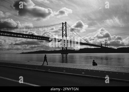 Silhouette de deux personnes se détendant au bord de la rivière sous un ciel nuageux et ensoleillé à Lisbonne, Portugal. Banque D'Images