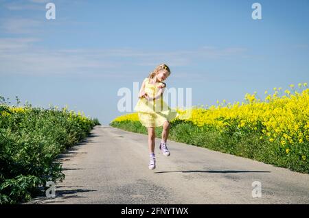 petite fille sautant parmi les champs de colza jaune en milieu rural vide chemin Banque D'Images