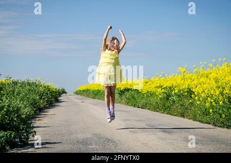 petite fille sautant parmi les champs de colza jaune en milieu rural vide chemin Banque D'Images