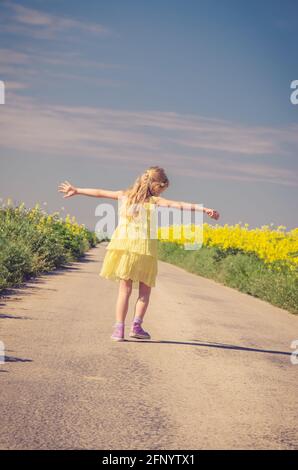 petite fille sautant parmi les champs de colza jaune en milieu rural vide chemin Banque D'Images