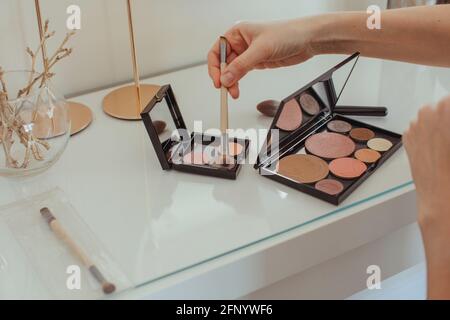 Gros plan de la main d'une femme en plongeant une brosse de maquillage dans le une palette de maquillage sur une coiffeuse Banque D'Images