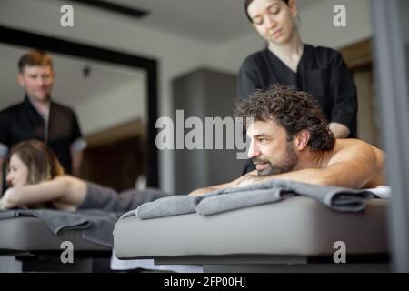 Beau couple allongé dans un salon de spa appréciant un massage profond du dos et de détente. Le bien-être et les loisirs pour les soins de santé ensemble. Concentrez-vous sur l'homme. Lumière naturelle. Banque D'Images