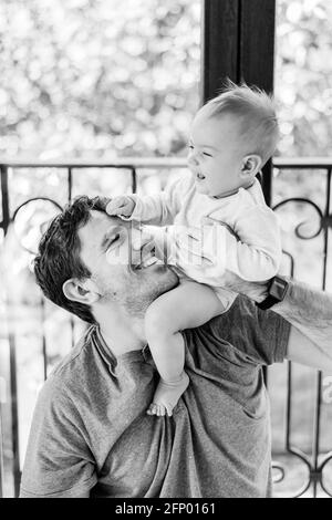 Un père souriant tient un bébé en train de rire dans un body blanc sur son épaule. Photo en noir et blanc Banque D'Images