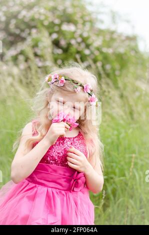 belle fille blonde en robe rose tenant fleur rose rose Banque D'Images