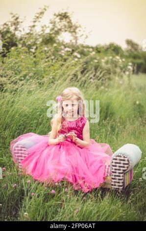 belle fille blonde en robe rose dans la prairie Banque D'Images