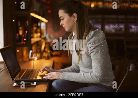 Une jeune fille est assise sur une chaise dans un café pour un ordinateur portable. Concept freelance. Banque D'Images