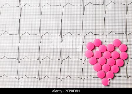 Une pile de pilules rouges en forme de coeur sur le cardiogramme. Concept médical. Banque D'Images