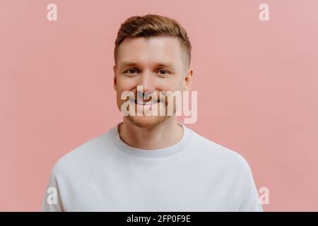 Jeune homme positif souriant à la caméra dans un arrière-plan rose studio Banque D'Images