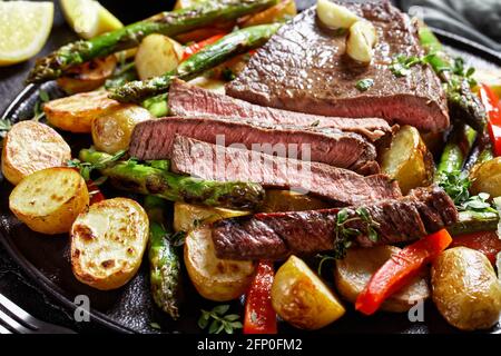 gros plan de steak de bœuf en tranches avec de nouvelles pommes de terre de légumes rôties, des asperges et du poivron rouge sur une assiette noire Banque D'Images