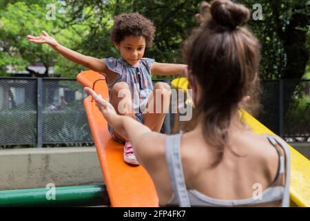 Fille de race mixte appréciant sa mère à l'aire de jeux à l'extérieur Banque D'Images