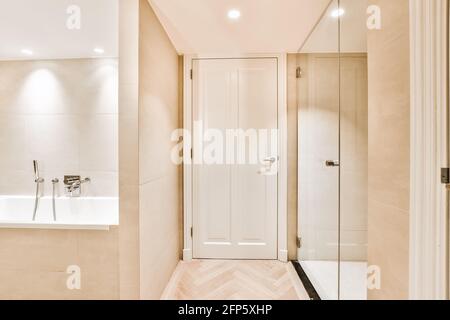 Porte classique blanche dans la salle de bains avec carrelage beige et lumineux éclairage équipé d'une cabine de douche et d'une baignoire blanche Banque D'Images