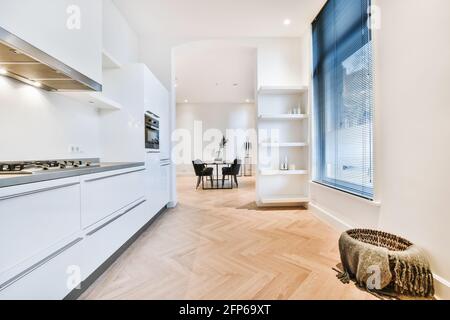 Intérieur de la maison salle de cuisine avec des armoires blanches minimalistes et appareils intégrés et passage ouvert à la salle à manger avec tableau Banque D'Images