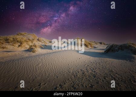 Image nocturne d'un paysage de dunes avec ciel étoilé et violet et une étoile violette sur fond bleu foncé du ciel Banque D'Images