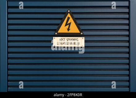Panneau de danger électrique sur un panneau triangulaire jaune monté sur une grille métallique bleu foncé avec le texte néerlandais « haute tension ». « dangereux » Banque D'Images