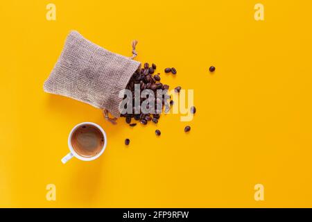 Il y a un petit sac ouvert et couché à partir duquel les grains de café tombent et se dispersent sur un fond jaune vu d'en haut. En bas se trouve une um blanche Banque D'Images