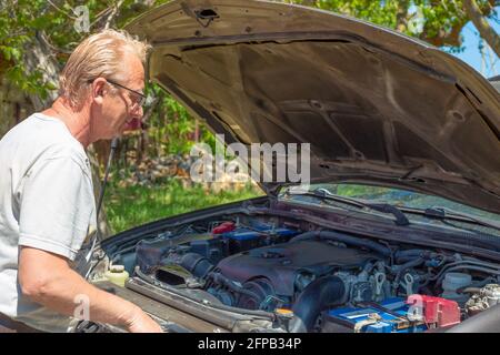 Un homme adulte blond européen âgé regarde sous le capot d'une voiture, essayant de faire face à un dysfonctionnement. Banque D'Images