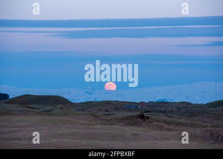 La pleine lune s'élève au-dessus du glacier islandais avec des collines ondoyantes le premier plan et le ciel bleu profond Banque D'Images