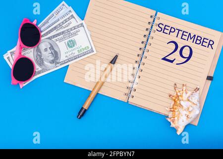 29e jour de septembre. Travel concept Flat lay - Bloc-notes avec la date du 29 septembre stylo, lunettes, dollars et seashell sur fond bleu. Automne m Banque D'Images