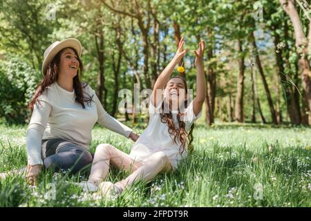 Mère et sa fille jouant à lancer des fleurs assis sur l'herbe dans le parc d'été. Détente en famille à l'extérieur Banque D'Images