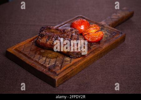 délicieux steak sur un os avec des tomates sur une planche de bois. Banque D'Images