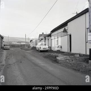 1960, historique, un vélo de tourisme se tenait à l'extérieur d'un bâtiment avec un panneau YHA dans le village de Litton Cheney, Dorset, Angleterre, Royaume-Uni. Une voiture Ford Anglia de l'époque est garée sur le bord du bâtiment. Un Mini clubman est garé à gauche de l'image. Banque D'Images