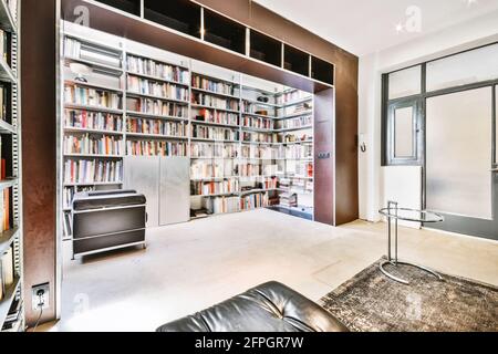 Décoration intérieure contemporaine, bibliothèque de luxe avec étagères forme de niche et chaise en cuir dans un appartement moderne Banque D'Images