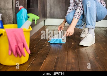 Les mains de femmes coupées balayant la poussière avec une brosse et une pelle, tenant le balai et le plancher de balayage, recueillant la poussière dans la pelle. Nettoyage des déchets.entretien ménager Banque D'Images