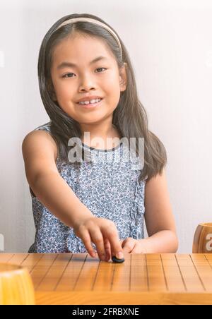 Portrait asiatique enfant fille joue aller avec le premier mouvement de la pierre noire. Le jeu de société chinois ou le jeu de société japonais, enfant regardant la caméra, sm Banque D'Images