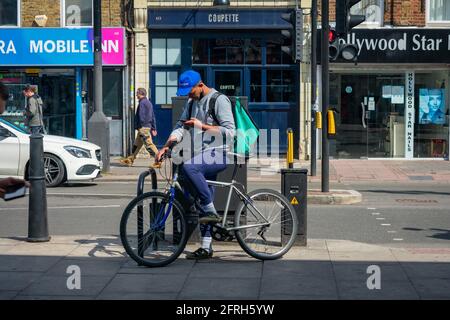 Londres. Royaume-Uni- 05.18.2021: Un jeune homme travaillant comme un travailleur indépendant de livraison à domicile pour la compagnie de commande de nourriture en ligne Deliveroo. Banque D'Images