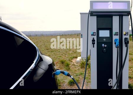 Voiture EV branchée sur le chargeur et la station de charge EV. Chargeur de voiture électrique près de l'autoroute. Voiture électrique. Charge de voiture à zéro émission. Sans carbone Banque D'Images