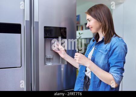 Distributeur d'eau, femme prenant l'eau froide dans le verre du réfrigérateur à la maison Banque D'Images