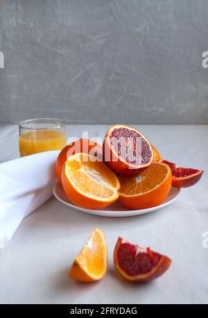 Oranges et oranges de sang sucrées et juteuses, entières et coupées sur une assiette blanche et des verres de jus d'orange frais. Banque D'Images