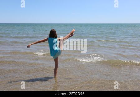 Une jeune fille athlétique lève sa jambe par la mer pendant exercices de gymnastique rythmique pour garder la forme pendant l'été Banque D'Images