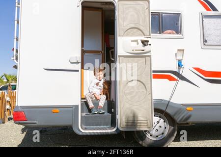 petit garçon aux cheveux bouclés souriant assis dans la porte de la maison de moteur, tenant tendement son animal de compagnie. Banque D'Images