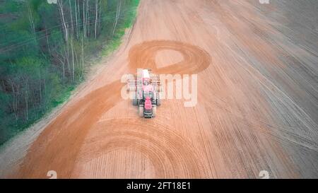 Le tracteur rouge effectue un demi-tour dans le champ et plère, cultive le champ le jour du printemps. Photo avec un drone Banque D'Images