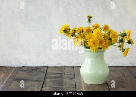 pissenlits lumineux, beaux et jaunes dans un vase sur une table en bois. fleurs jaunes printanières ou estivales sur fond texturé gris. arrière-plan avec espace de copie. Banque D'Images