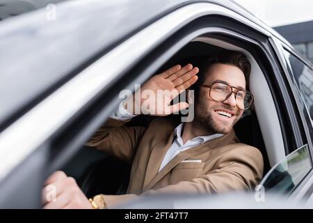 homme heureux dans des lunettes regardant à travers la fenêtre de voiture et de passage main pendant la conduite automatique Banque D'Images