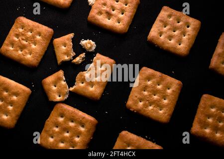 Biscuits savoureux soigneusement disposés en rangées, avec un biscuit cassé, sur un fond noir Banque D'Images