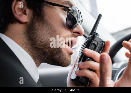 gros plan de la protection du corps barbu dans des lunettes de soleil à l'aide d'un talkie-walkie en voiture Banque D'Images