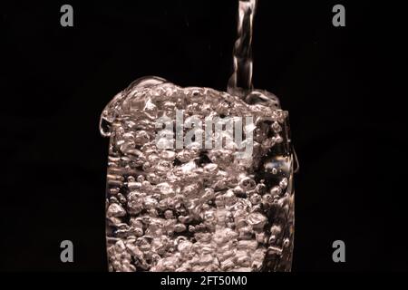 Gros plan de l'eau potable fraîche est versé dans un verre sur fond noir Banque D'Images